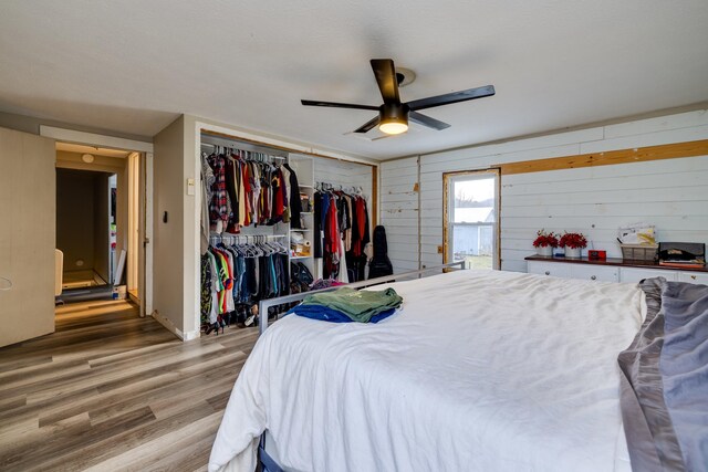 bedroom featuring wood-type flooring, wooden walls, ceiling fan, and a closet