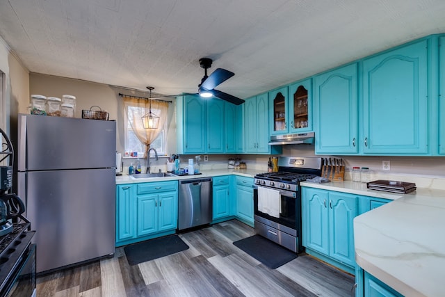 kitchen with blue cabinetry, sink, light stone counters, hanging light fixtures, and stainless steel appliances