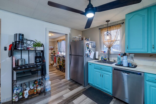 kitchen featuring blue cabinetry, sink, decorative light fixtures, light wood-type flooring, and appliances with stainless steel finishes