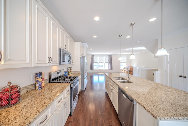 kitchen with pendant lighting, sink, white cabinets, stainless steel appliances, and a center island with sink