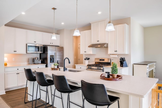 kitchen with stainless steel appliances, a kitchen island with sink, sink, and hanging light fixtures