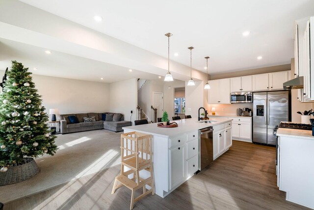 kitchen featuring decorative light fixtures, white cabinetry, hardwood / wood-style flooring, a kitchen island with sink, and stainless steel appliances