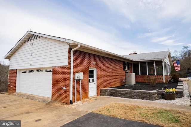 view of home's exterior featuring an attached garage, central AC, brick siding, a sunroom, and concrete driveway