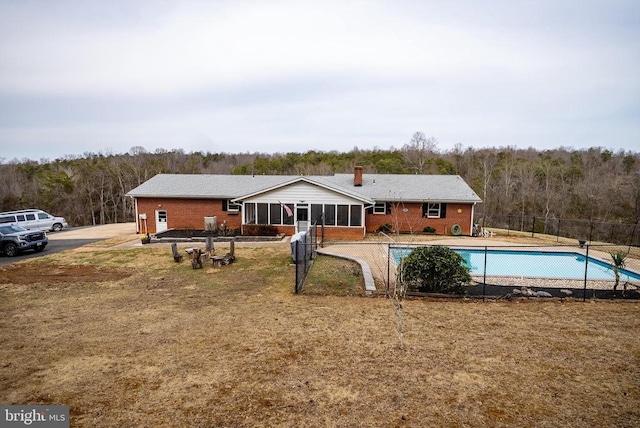 rear view of property featuring brick siding, fence, a sunroom, a fenced in pool, and a wooded view