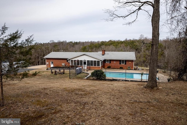 back of house with a fenced in pool, a sunroom, brick siding, and a wooded view