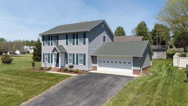 colonial-style house featuring an attached garage, a front lawn, aphalt driveway, and roof with shingles