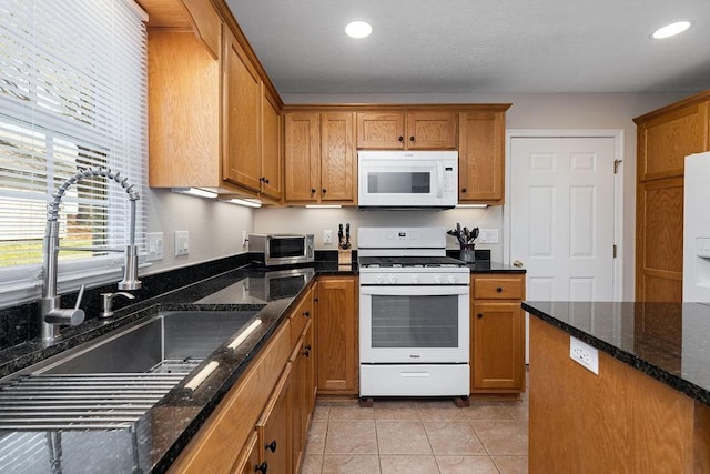 kitchen with dark stone countertops, white appliances, a sink, and brown cabinets