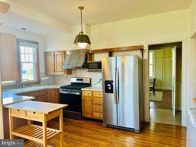 kitchen featuring a sink, wall chimney range hood, dark wood-style floors, appliances with stainless steel finishes, and light countertops