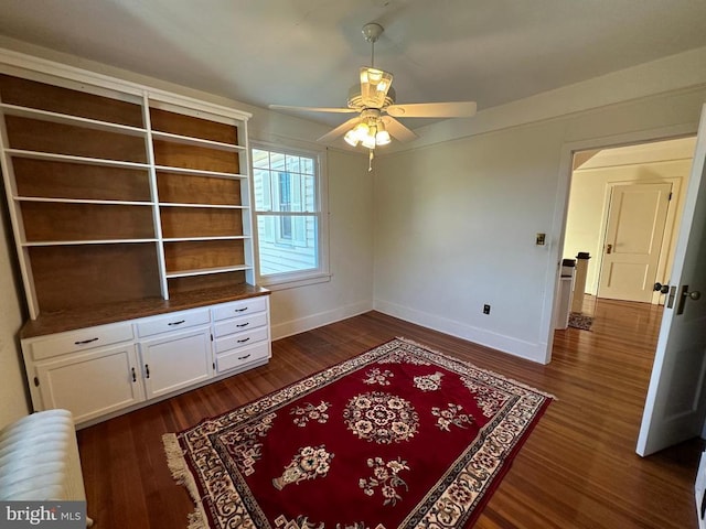 interior space with baseboards, ceiling fan, and dark wood-style flooring