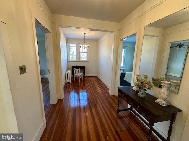 corridor with baseboards, radiator, an inviting chandelier, and wood finished floors