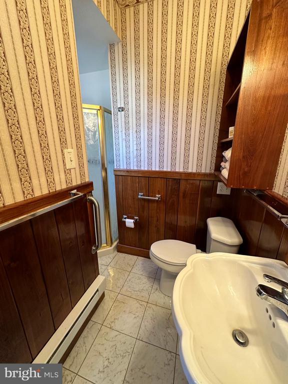 bathroom featuring wallpapered walls, toilet, wainscoting, a stall shower, and a sink