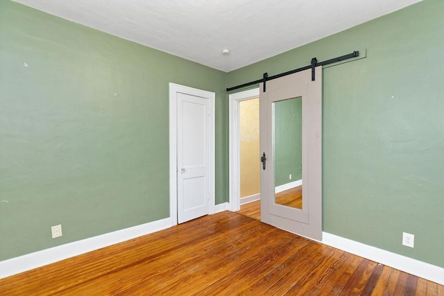 unfurnished room with a barn door, baseboards, and wood finished floors