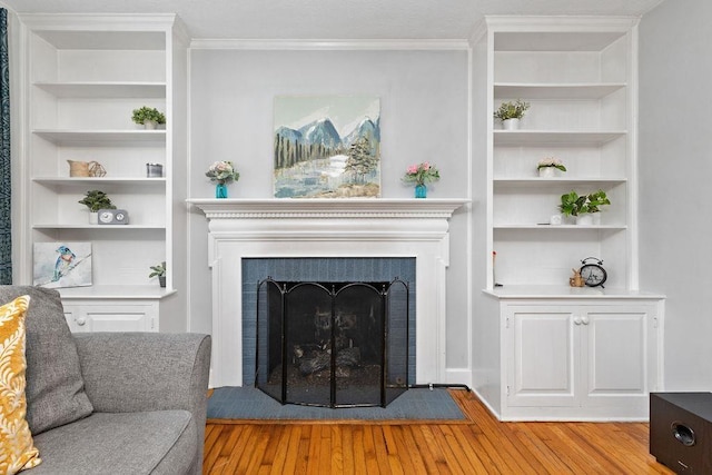 living room with built in shelves, a fireplace, wood-type flooring, and ornamental molding