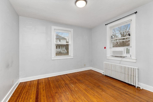 empty room featuring a wealth of natural light, radiator, baseboards, and wood finished floors