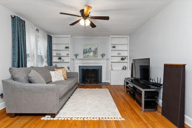 living area featuring ceiling fan, a fireplace, wood-type flooring, and a textured ceiling