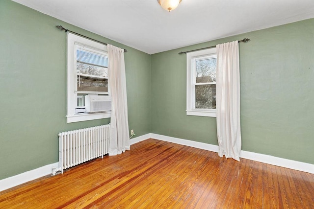 spare room featuring cooling unit, radiator, baseboards, and wood finished floors