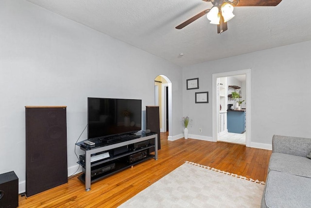 living room featuring a ceiling fan, a textured ceiling, wood finished floors, arched walkways, and baseboards