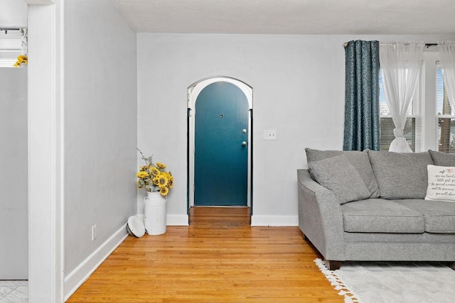 living area with light wood-style floors, baseboards, and arched walkways