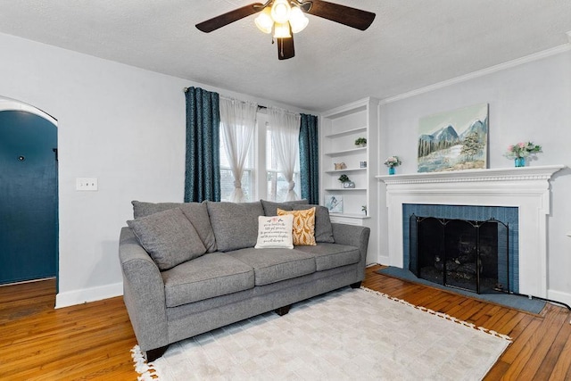 living area with built in shelves, a textured ceiling, hardwood / wood-style floors, arched walkways, and baseboards