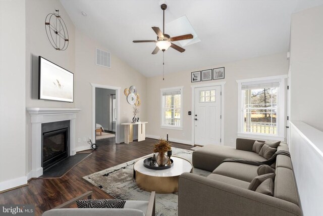 living room with visible vents, a ceiling fan, a glass covered fireplace, baseboards, and dark wood-style flooring