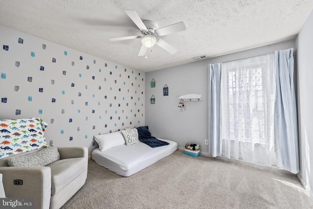 carpeted bedroom featuring visible vents, ceiling fan, a textured ceiling, baseboards, and wallpapered walls