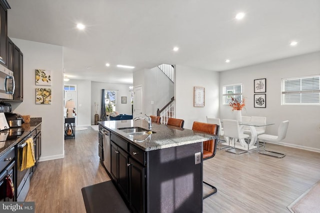 kitchen featuring sink, stainless steel appliances, a kitchen breakfast bar, light stone counters, and a center island with sink