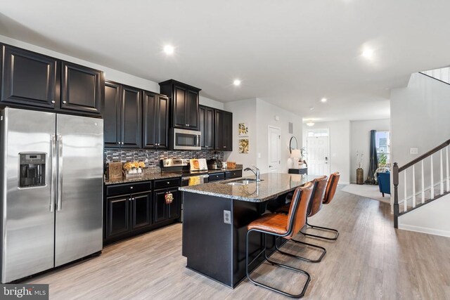 kitchen featuring sink, a kitchen breakfast bar, an island with sink, stainless steel appliances, and light stone countertops