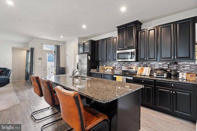 kitchen with an island with sink, stainless steel appliances, a breakfast bar, and sink