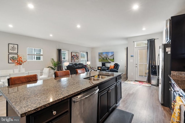 kitchen featuring stainless steel dishwasher, sink, a center island with sink, and dark stone countertops