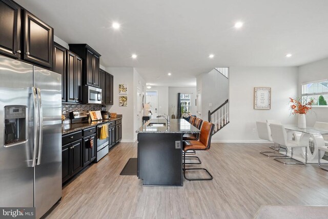 kitchen featuring sink, a kitchen breakfast bar, stainless steel appliances, light stone countertops, and a kitchen island with sink