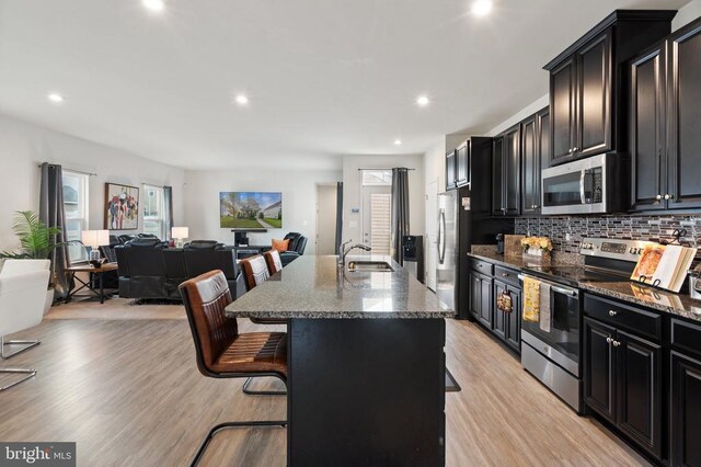 kitchen with a kitchen bar, sink, dark stone counters, an island with sink, and stainless steel appliances