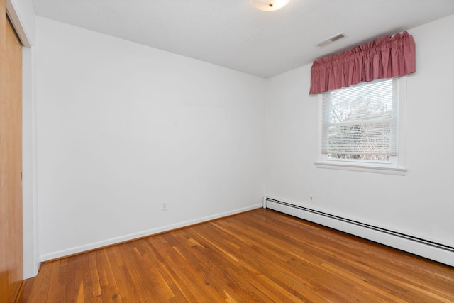 empty room featuring wood-type flooring, baseboards, visible vents, and baseboard heating