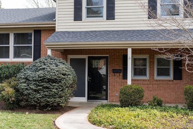 view of exterior entry featuring brick siding and a shingled roof