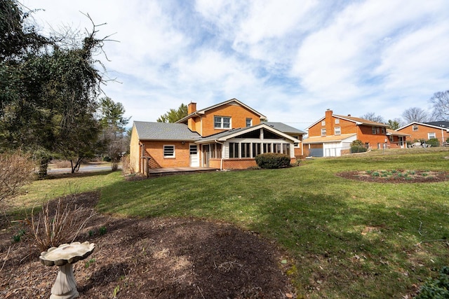 back of property featuring a deck, a yard, a sunroom, brick siding, and a chimney