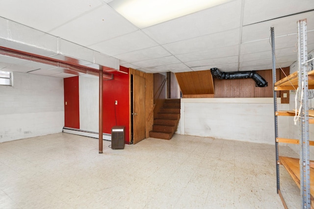 finished below grade area with stairway, wooden walls, a baseboard radiator, a paneled ceiling, and tile patterned floors