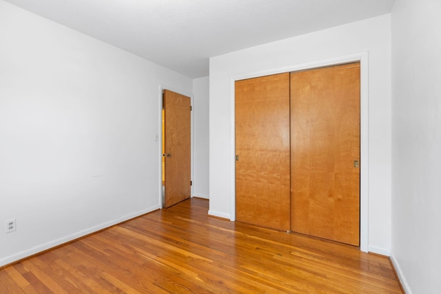 unfurnished bedroom featuring a closet, baseboards, and light wood finished floors