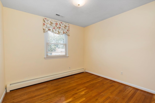 spare room featuring a baseboard heating unit, wood finished floors, visible vents, and baseboards