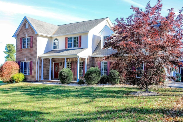 view of front of house featuring brick siding, a porch, a front yard, and a shingled roof