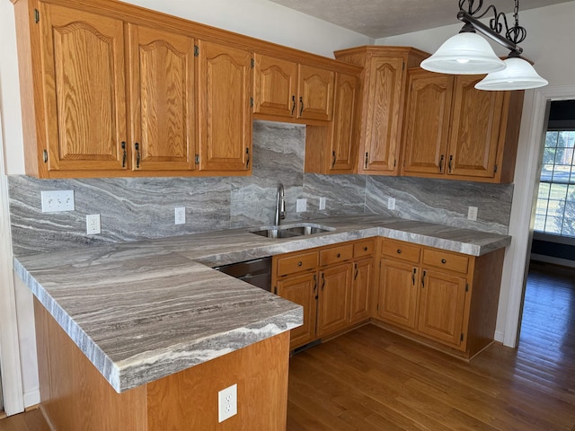 kitchen with brown cabinets, dark wood-type flooring, decorative light fixtures, a peninsula, and a sink