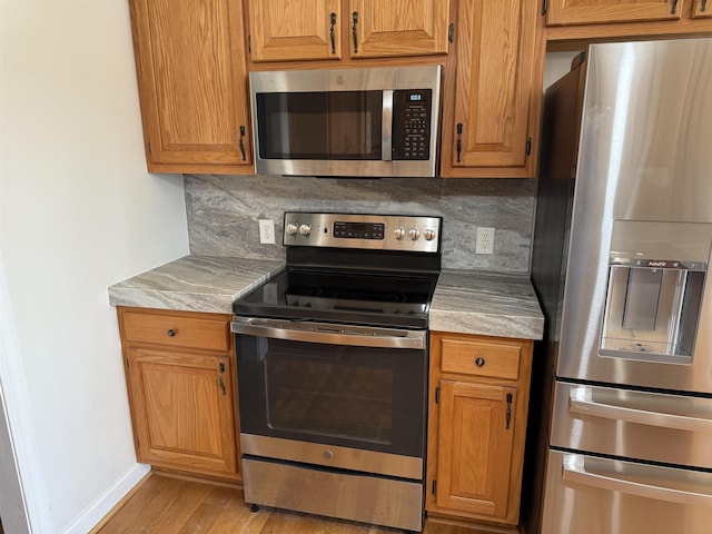 kitchen featuring stainless steel appliances, baseboards, light countertops, brown cabinets, and tasteful backsplash