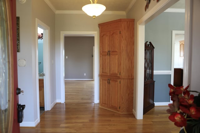 corridor with light wood-style floors, crown molding, and baseboards