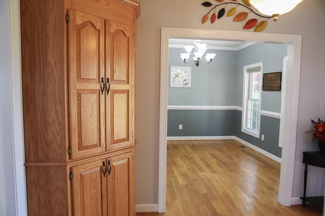 hall featuring light wood finished floors, visible vents, baseboards, crown molding, and a notable chandelier