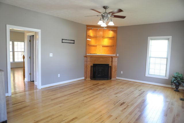 unfurnished living room featuring ceiling fan, a fireplace with flush hearth, light wood-style flooring, and baseboards