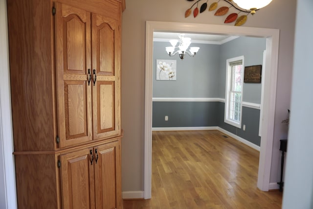 hall featuring ornamental molding, light wood-type flooring, a notable chandelier, and baseboards