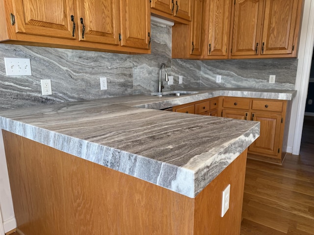 kitchen with brown cabinets, a sink, a peninsula, and decorative backsplash