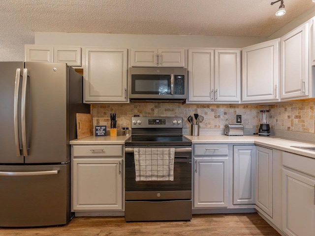 kitchen featuring white cabinetry, stainless steel appliances, tasteful backsplash, and light wood-type flooring