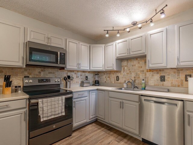 kitchen featuring appliances with stainless steel finishes, white cabinetry, sink, light wood-type flooring, and a textured ceiling