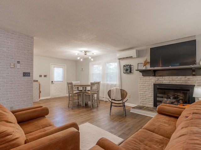 living room featuring wood-type flooring, a fireplace, a wall mounted AC, and a textured ceiling