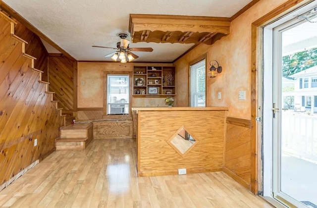 bar featuring crown molding, ceiling fan, light hardwood / wood-style floors, a textured ceiling, and wood walls