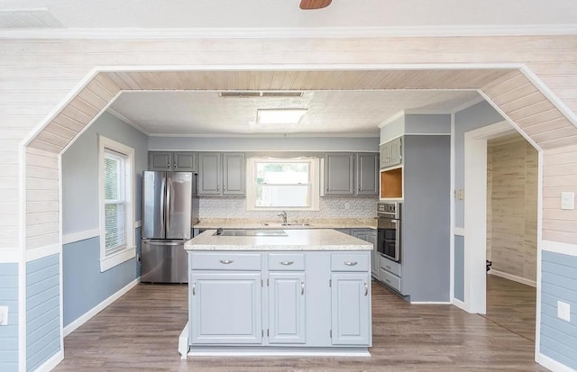 kitchen featuring wood-type flooring, a center island, ornamental molding, gray cabinets, and stainless steel appliances